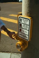 Person pressing crosswalk button on - Credits: pexels