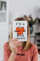 Woman concealing face with book - Credits: pexels