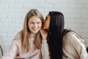 Two teenage girls whispering indoors, - Credits: pexels