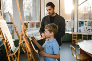 Art teacher supervises child painting - Credits: pexels