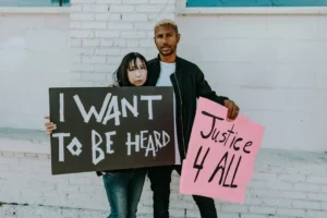 Two individuals holding protest signs - Credits: pexels