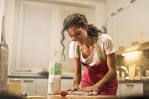 Smiling woman making dough at - Credits: pexels