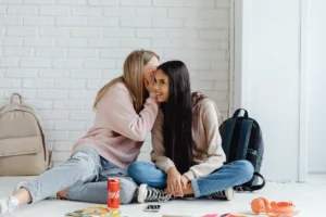 Two teenage girls whispering and - Credits: pexels