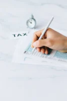 Hand completing tax forms with - Credits: pexels